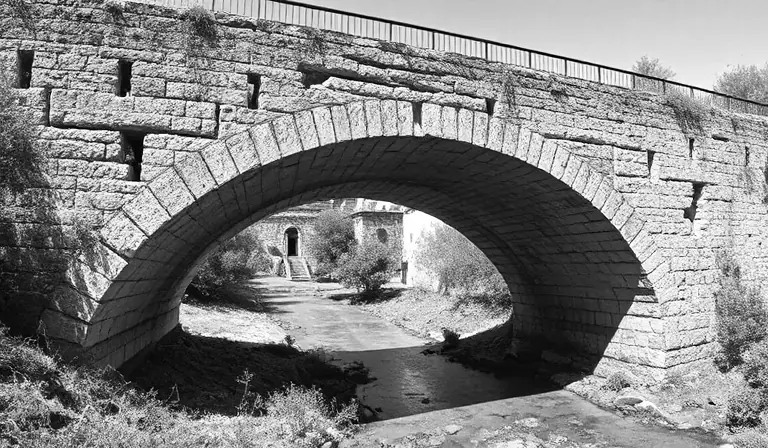Ancien pont de pierre fissuré au-dessus d’un canal asséché.