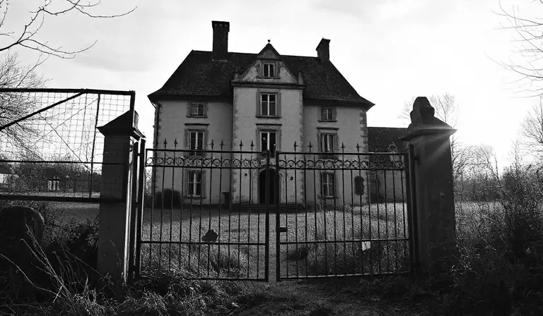 Château rural déserté, entouré d’un fossé envahi par les herbes et de façades dégradées.