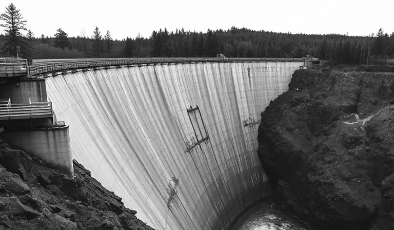 Ancien barrage monumental en béton, envahi par la végétation dans une gorge boisée.
