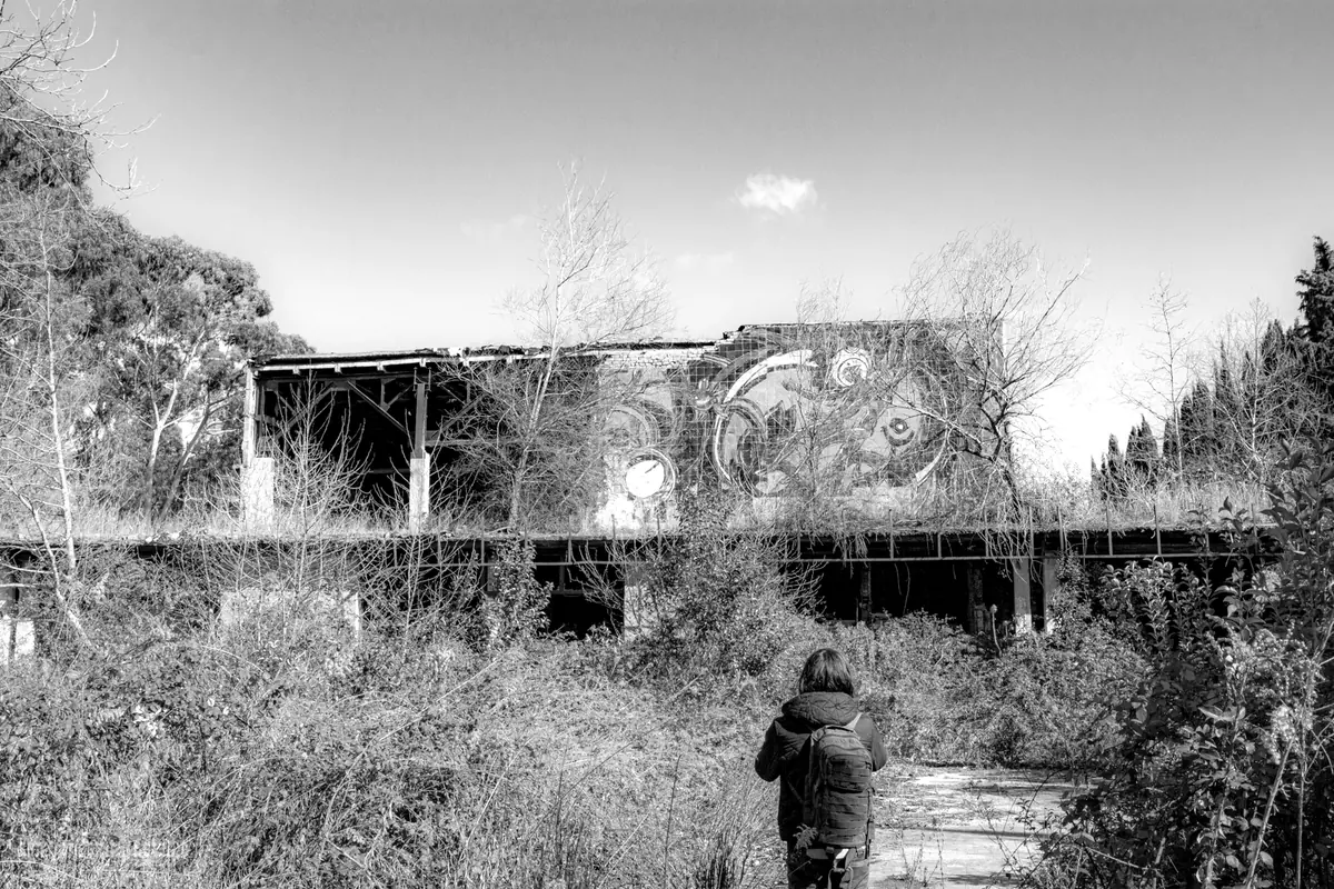 Un explorateur, sac sur le dos, marche vers un bâtiment abandonné envahi par la végétation
